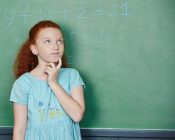 Grübelndes Mädchen löst Rechenaufgabe an der Tafel in der Grundschule