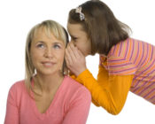 10-12yo girl is whispering to mother's ear. Isolated on white in studio.